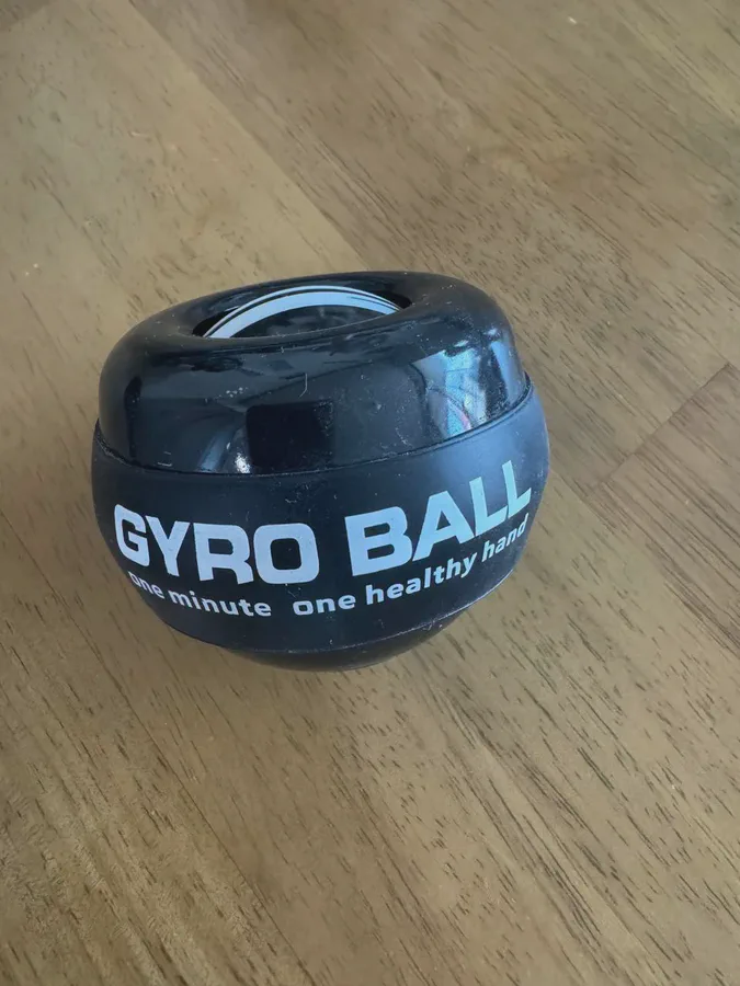 나무 책상 위에 놓인 검은색 자이로볼. 겉면에 GYRO BALL 문구가 인쇄된 고무 밴드가 감겨 있다